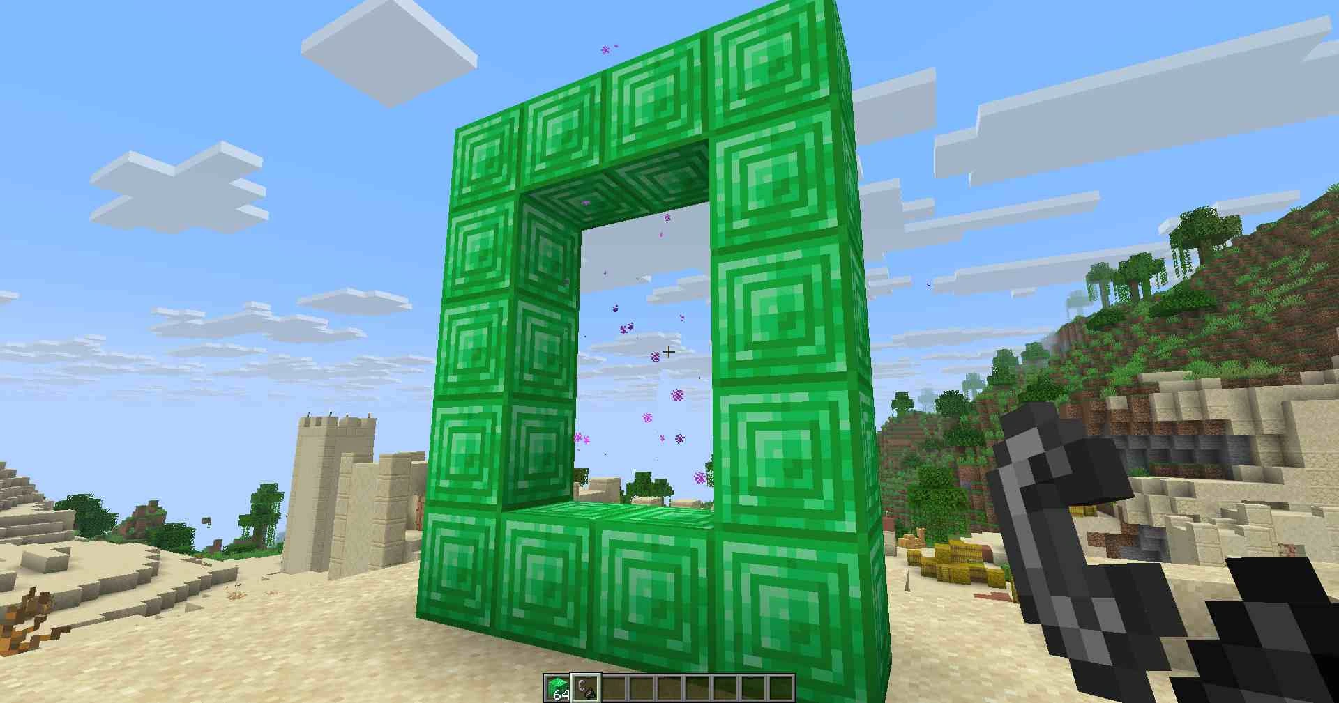 A hollow rectangular frame of emerald blocks near a desert structure, glowing with swirling portal particles